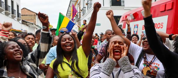 Diverse crowd of young people in a street with raised fists and flags.