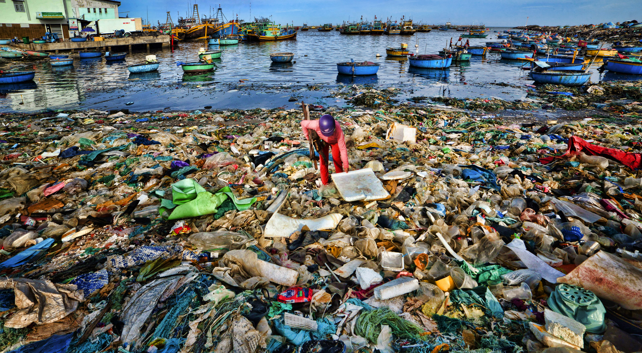 Man stoops over plastic beach waste