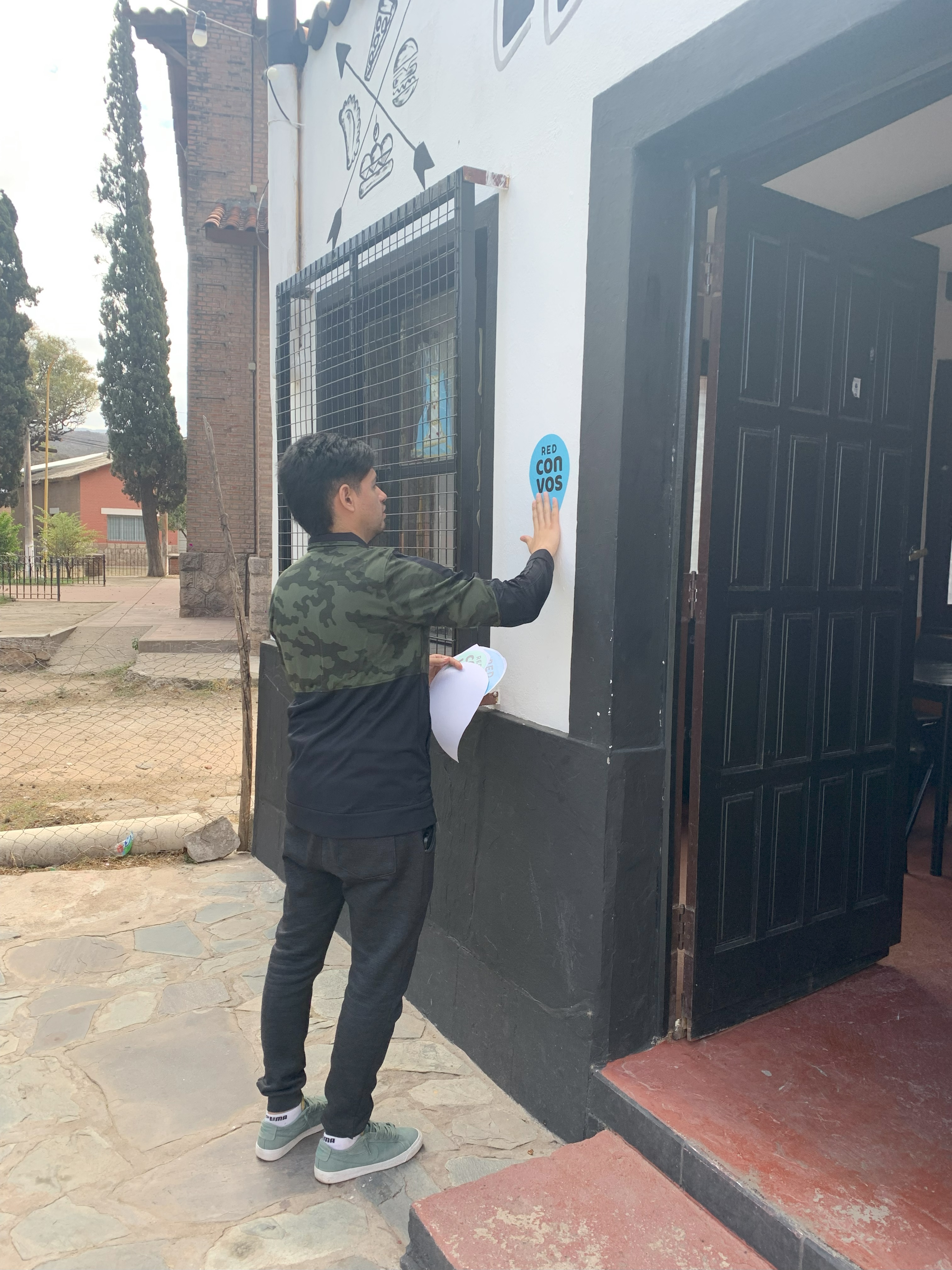 A man putting a 'Con Vos' sticker on a wall beside a door