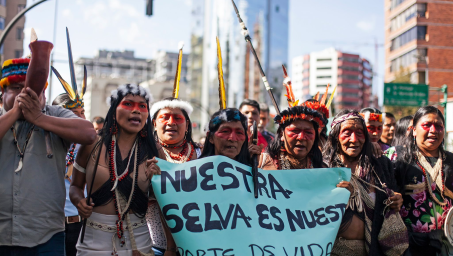 Indigenous activists march in streets carrying banner in Spanish