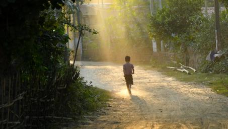 Child walking along a path with sun shining through trees