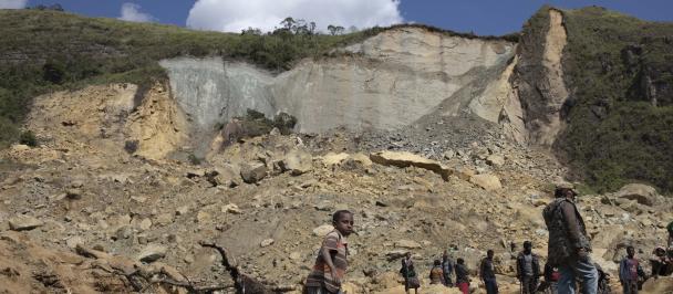 Wide shot of collapsed hillside with people walking over rubble